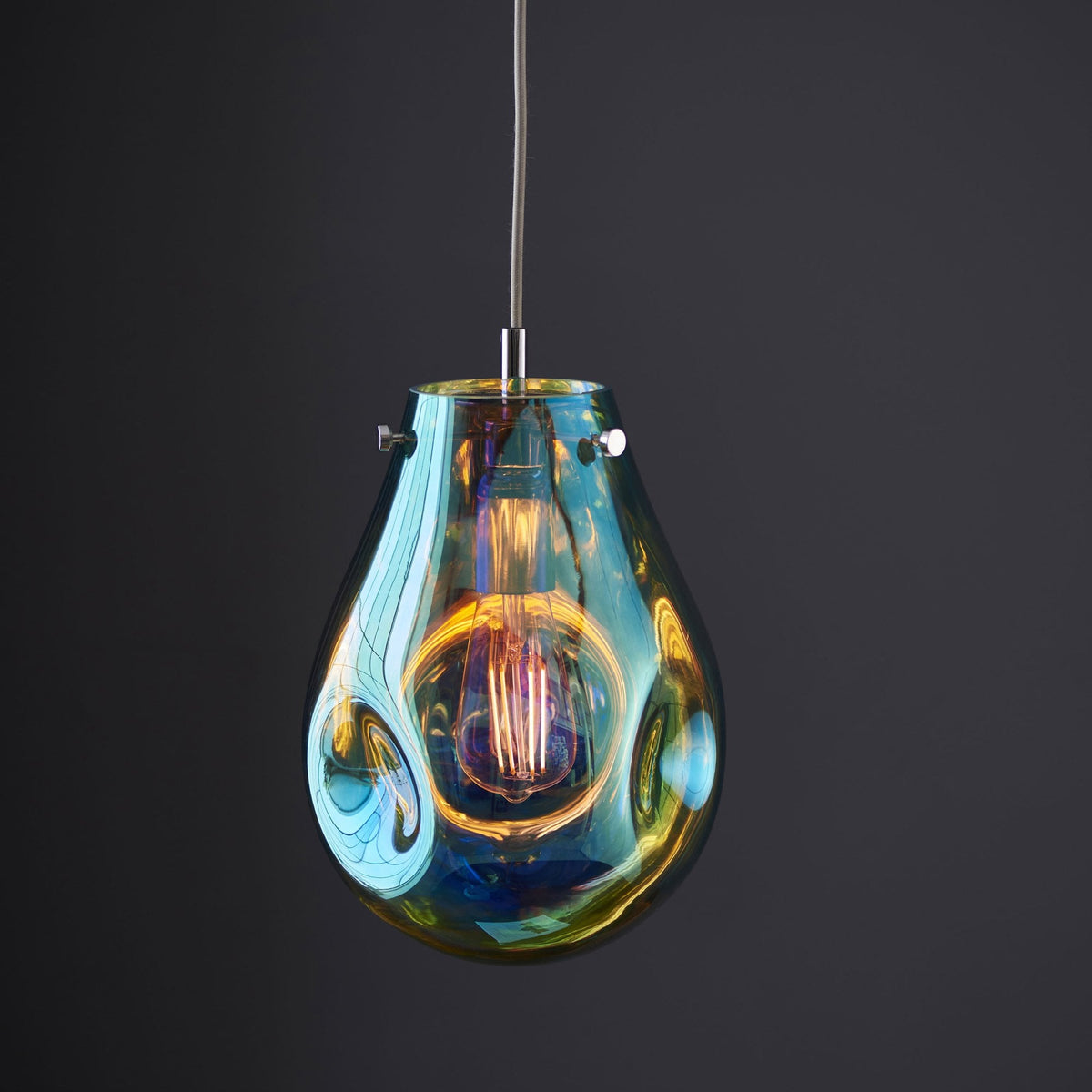 Teardrop pendant light in iridescent blue and amber with a lit filament bulb.
