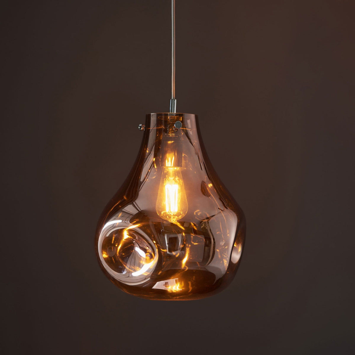 A single, illuminated bronze glass pendant light with a unique, organic, melting shape against a dark background.