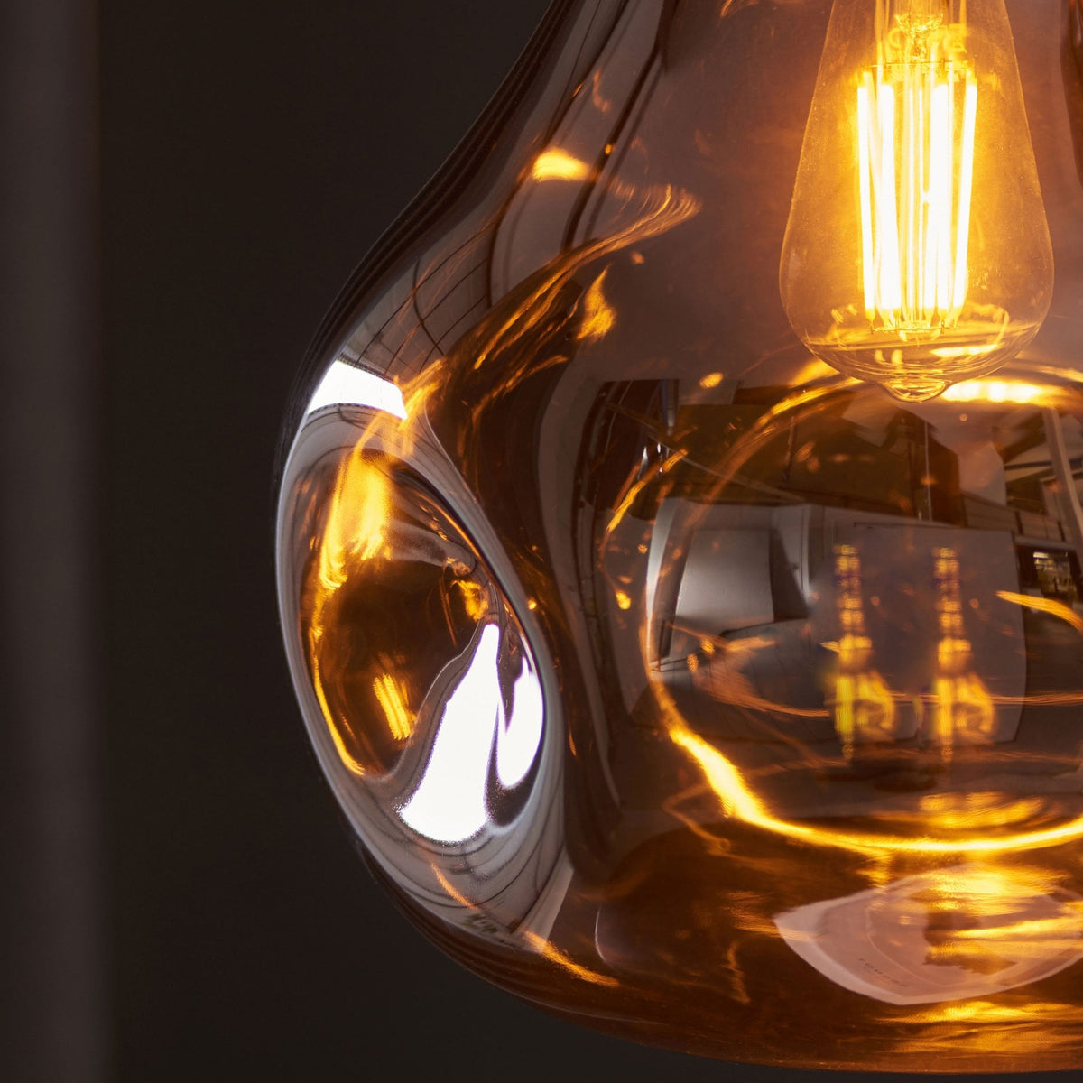 A close-up of an illuminated bronze glass pendant light, highlighting its textured, molten-like surface.