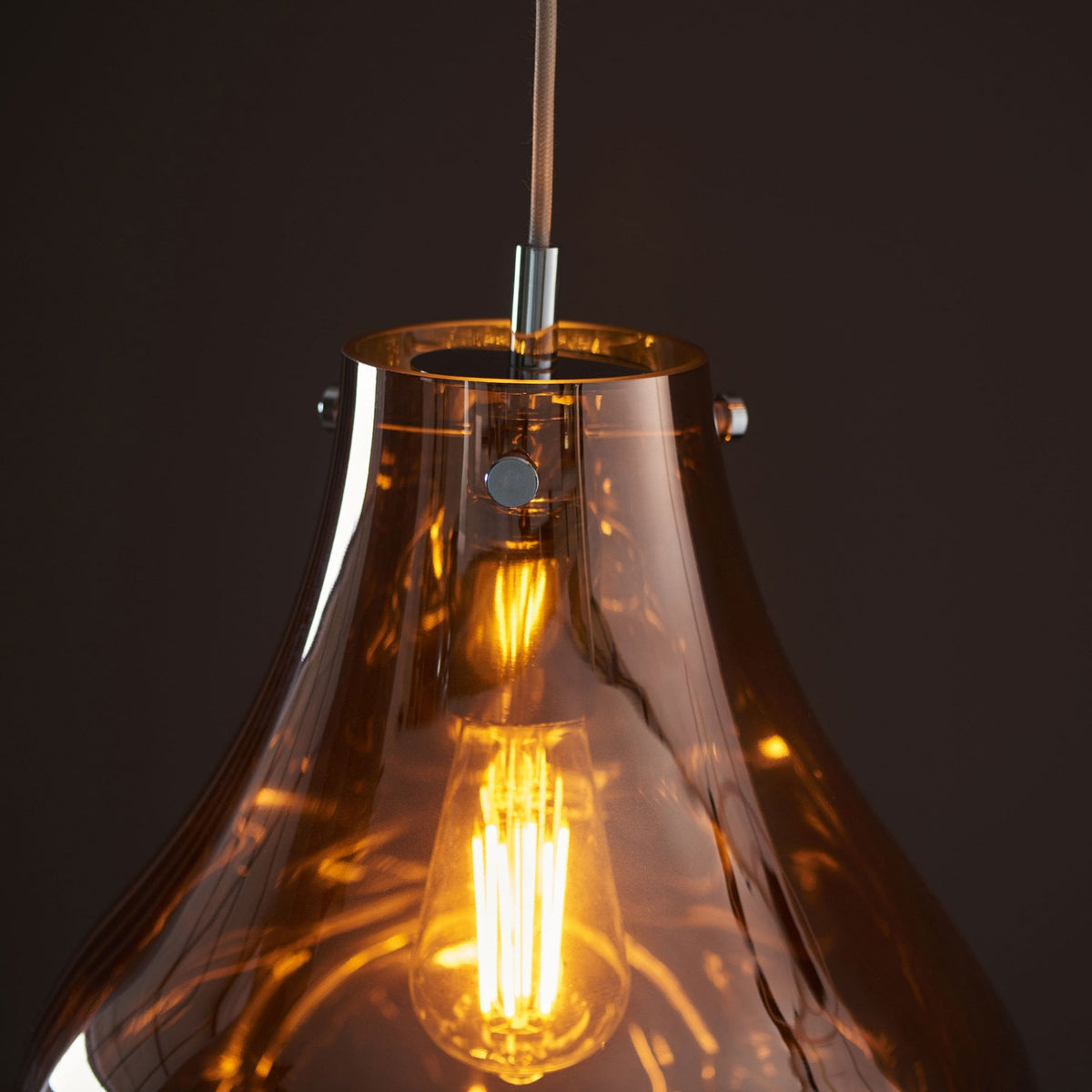 A close-up of the top of an illuminated bronze glass pendant light, showing the light fixture and bulb.
