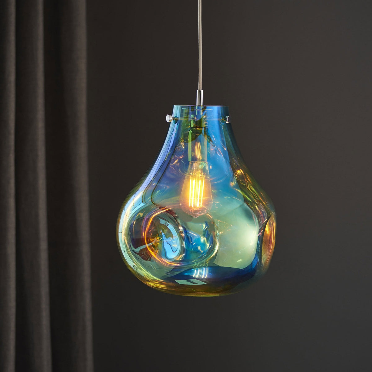 Iridescent glass pendant light, teardrop shape with a visible bulb, against a dark curtain.