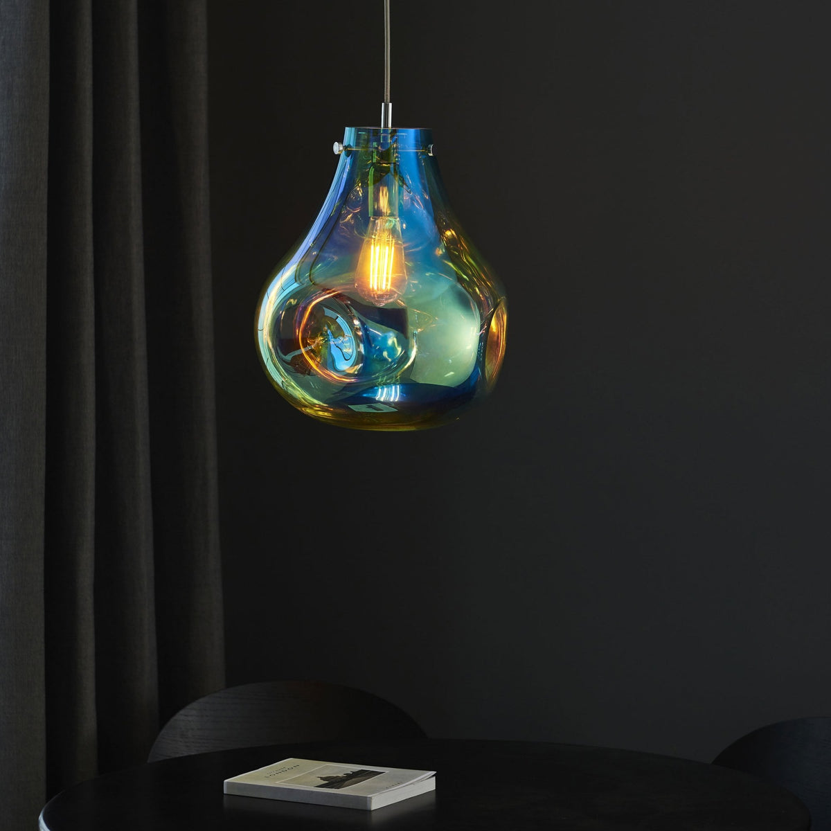 Iridescent glass pendant light illuminates a dark dining table with a book.