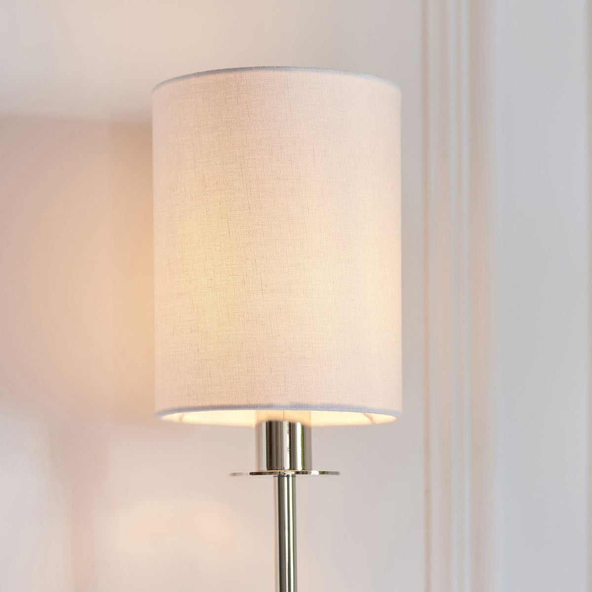 Close-up of a white fabric drum shade on a polished nickel wall sconce, casting a warm glow.