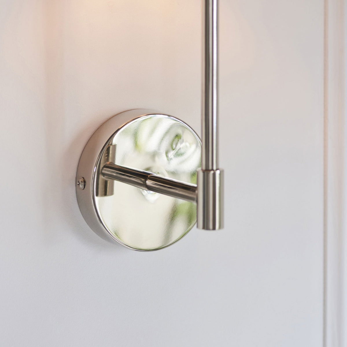 Close-up of the polished nickel base of a wall sconce, reflecting its surroundings.
