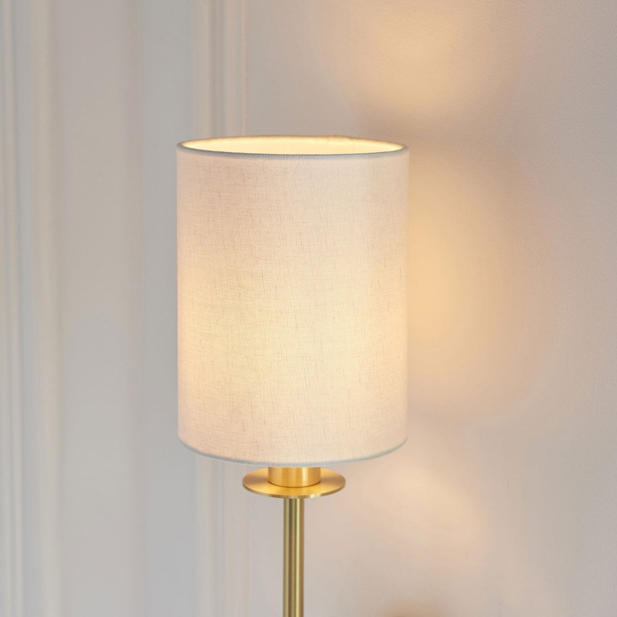 Close-up of the white fabric shade and brass details of a stylish wall sconce, emitting a soft light.