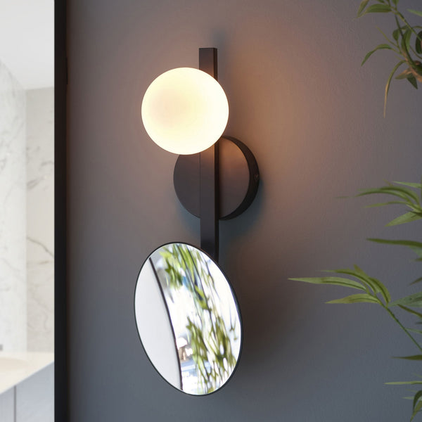 Modern black wall light with a spherical glass shade and a circular mirror attached.
