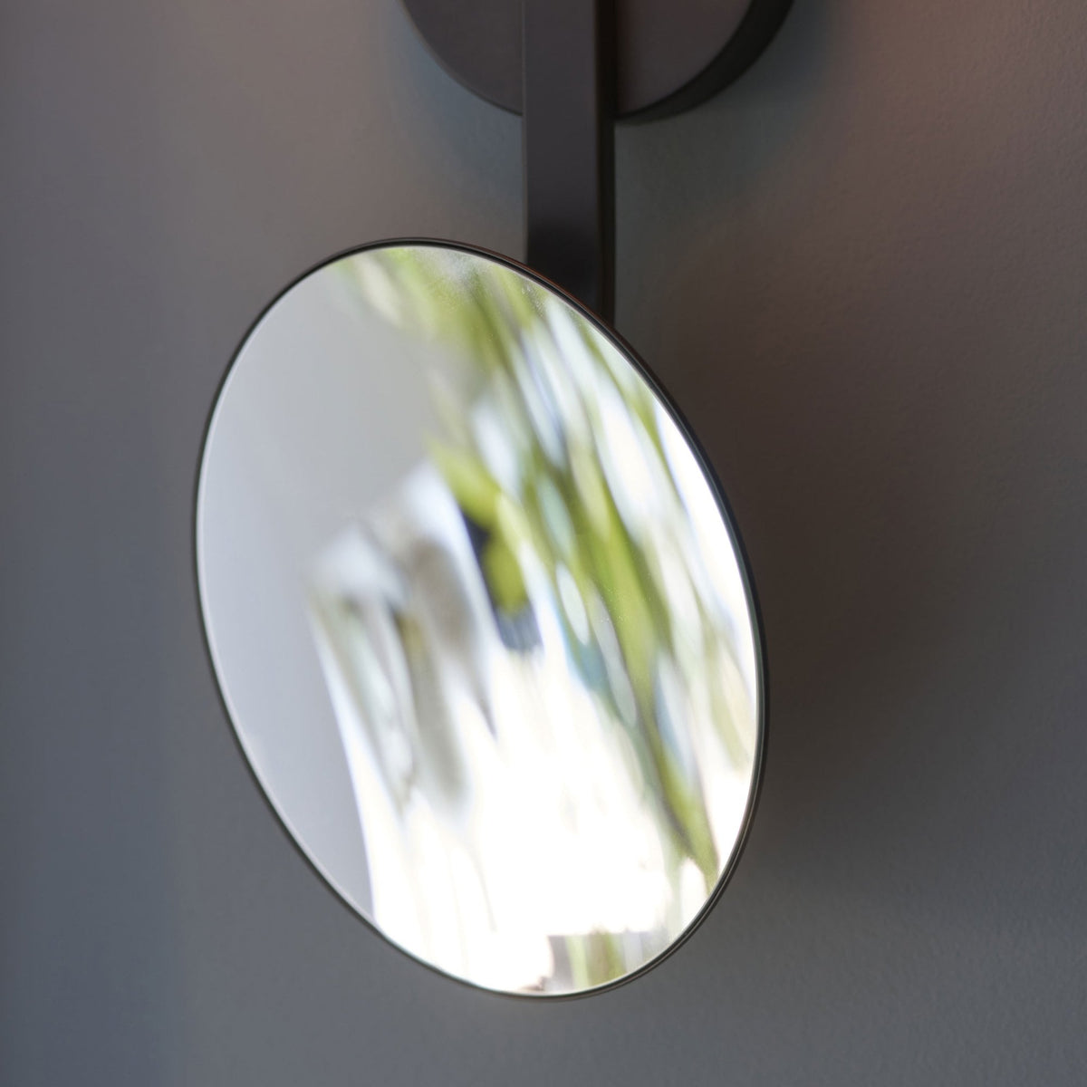 Close-up of the circular mirror attachment on the modern black wall light.