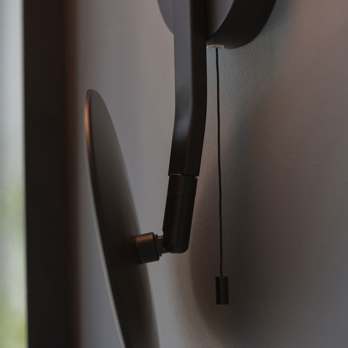 Close-up of the adjustable arm and pull switch on the modern black wall light.
