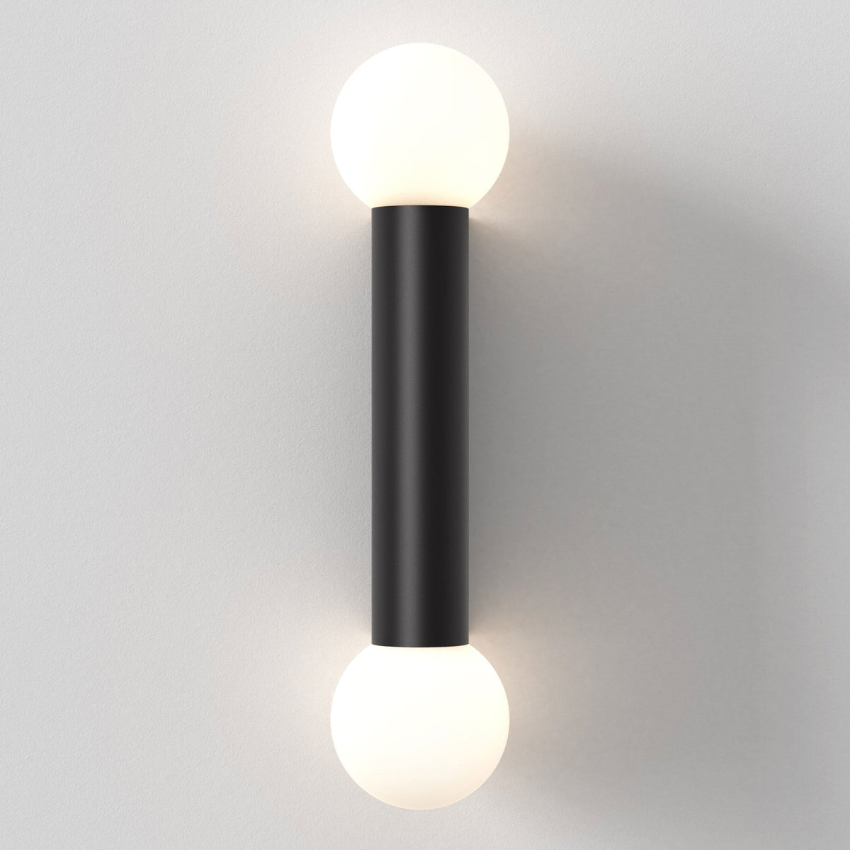 Black cylindrical wall sconce with two spherical white lights, one at each end, against a white wall