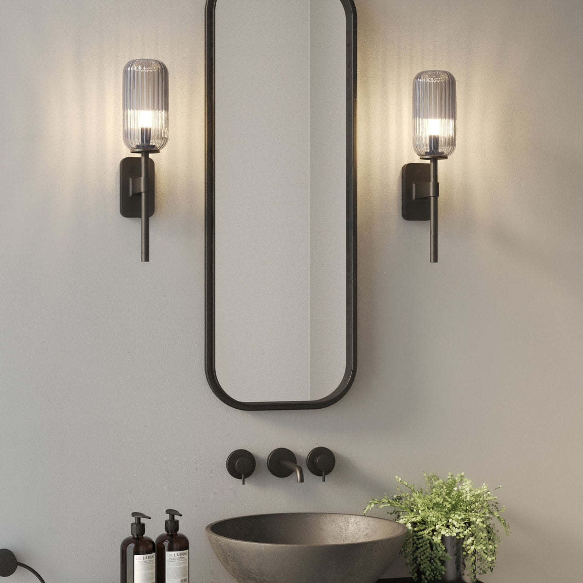 Bathroom vanity with a black mirror, two wall sconces, a dark basin, and a green plant