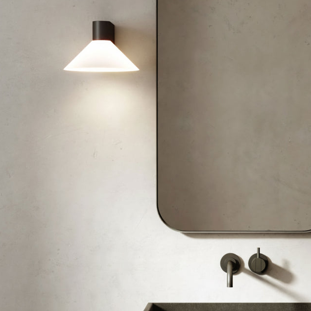 Wall-mounted light fixture with a conical white shade and a dark base, illuminating a textured wall