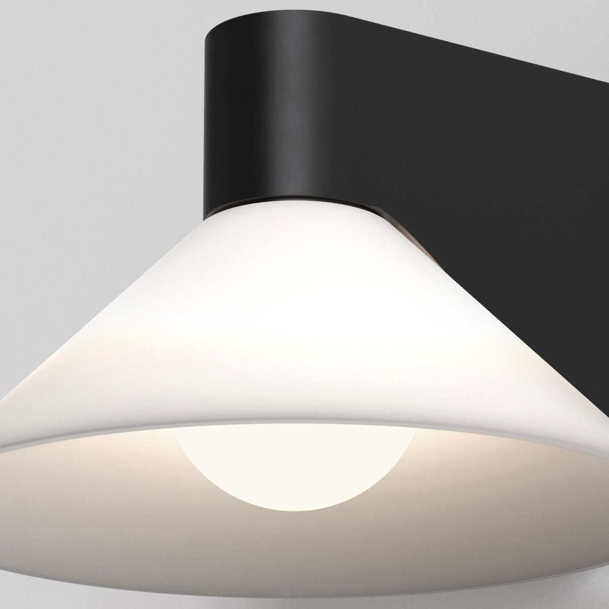 Close up of a black wall-mounted light fixture with a white conical shade and a glowing bulb