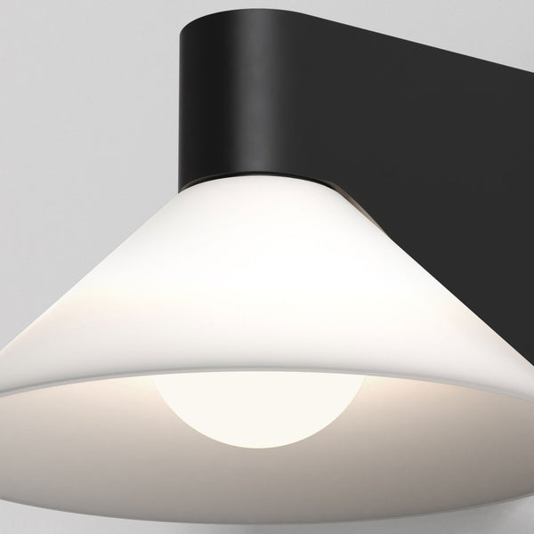 Close up of a black wall-mounted light fixture with a white conical shade and a glowing bulb