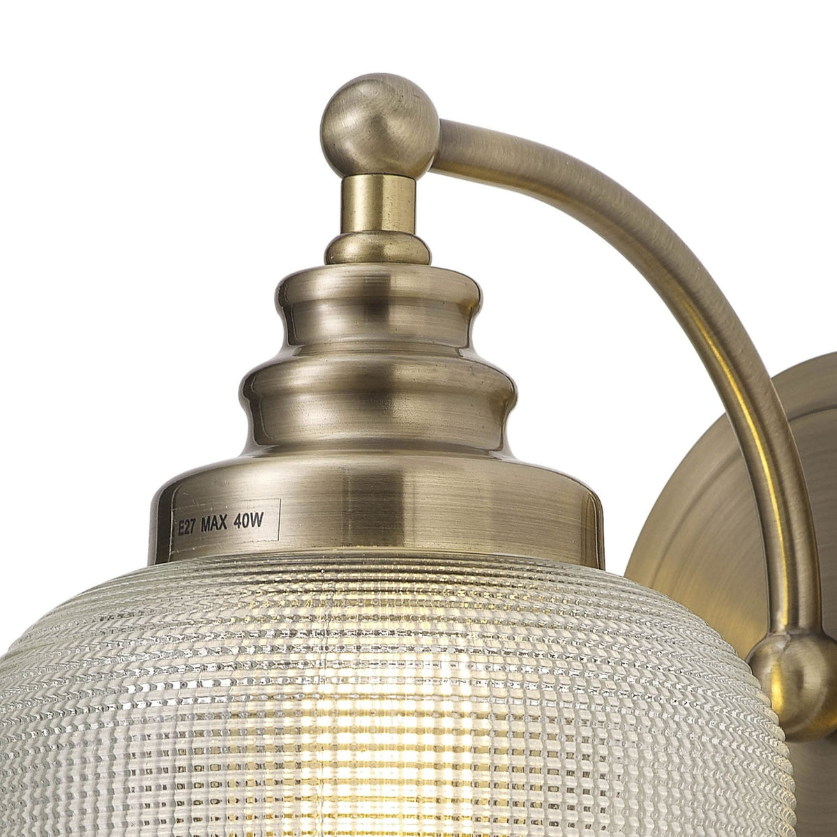 Close-up of the brass base and textured glass shade of a wall light, partially lit.