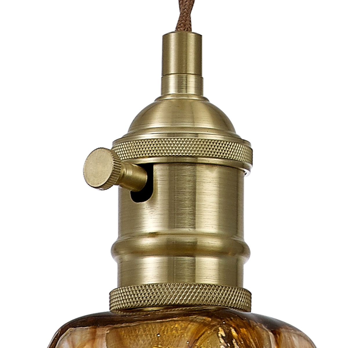 Close up of a brass light fixture with a brown braided cord and a textured amber glass shade