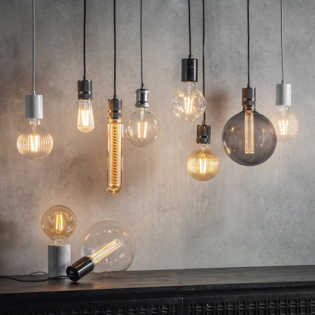 Assortment of pendant lights and bulbs in various shapes and sizes on a dark surface.