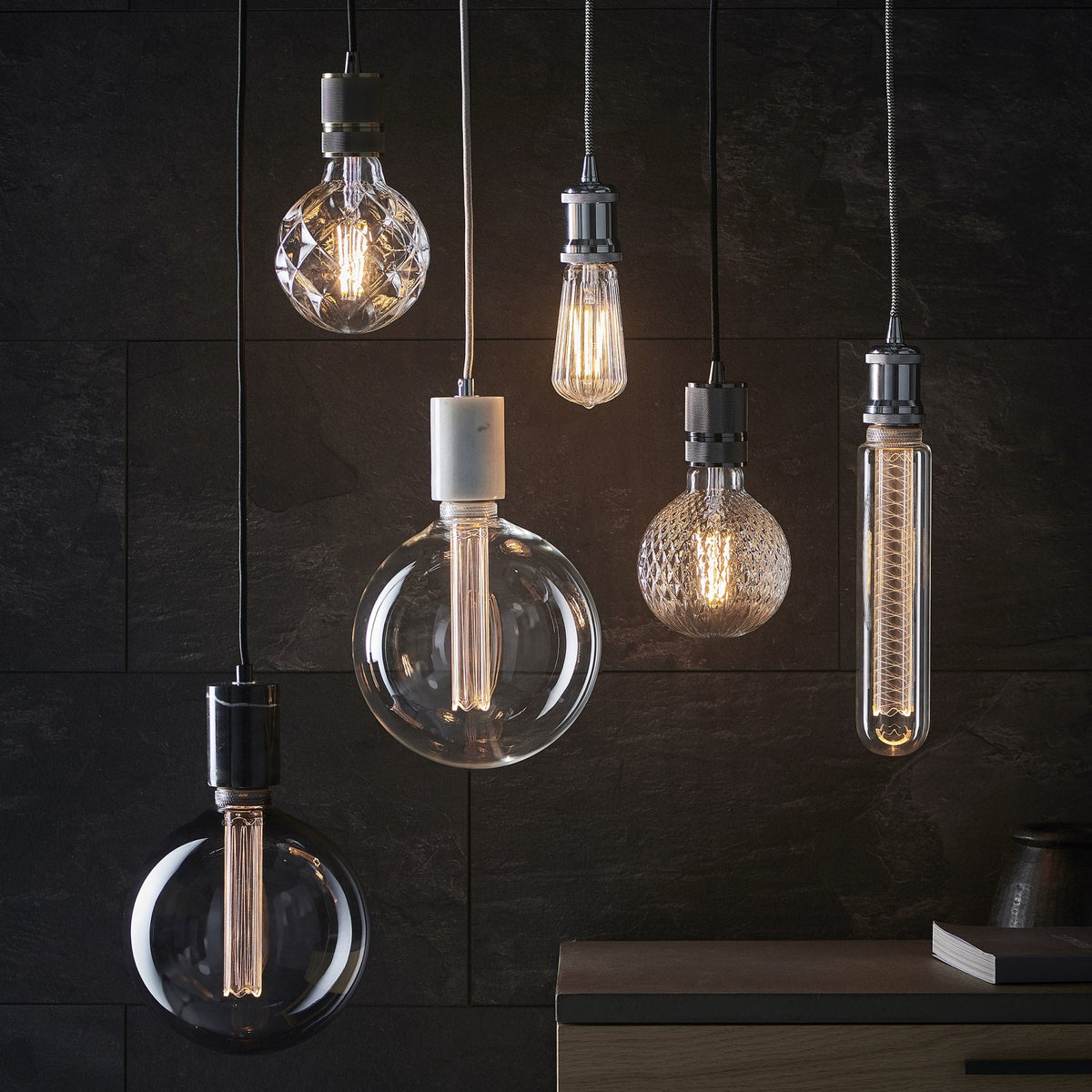 Collection of pendant lights with different bulb shapes and textures against a dark wall.