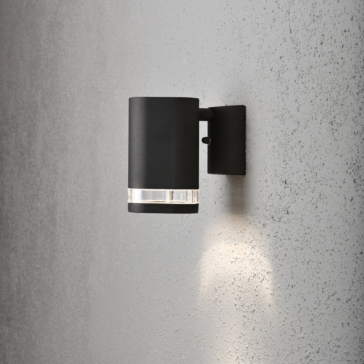 Black cylindrical outdoor wall light with clear band, mounted on a textured grey wall