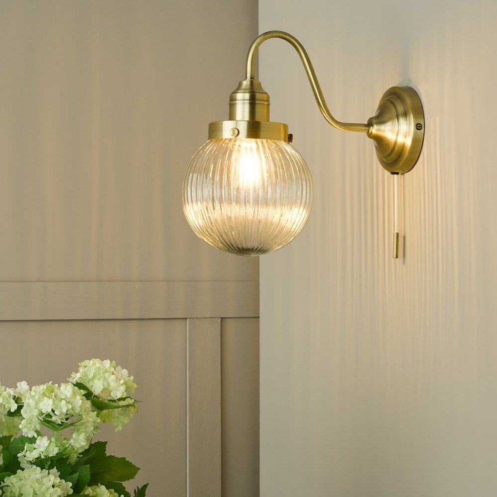 A brass wall light with a ribbed glass globe shade and a pull cord switch.