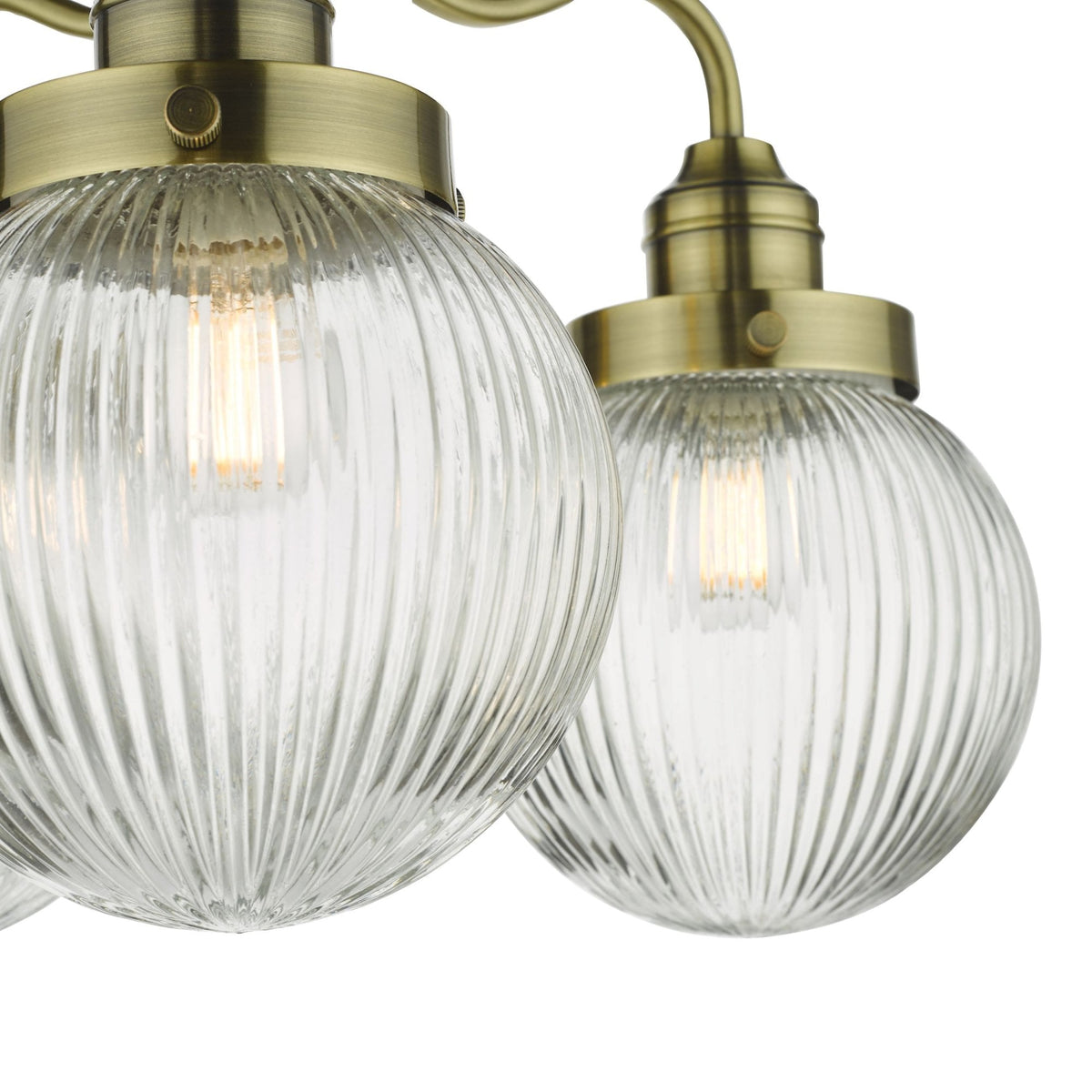 Close-up of two ribbed glass globe light fixtures with brass accents, illuminated against a white background.