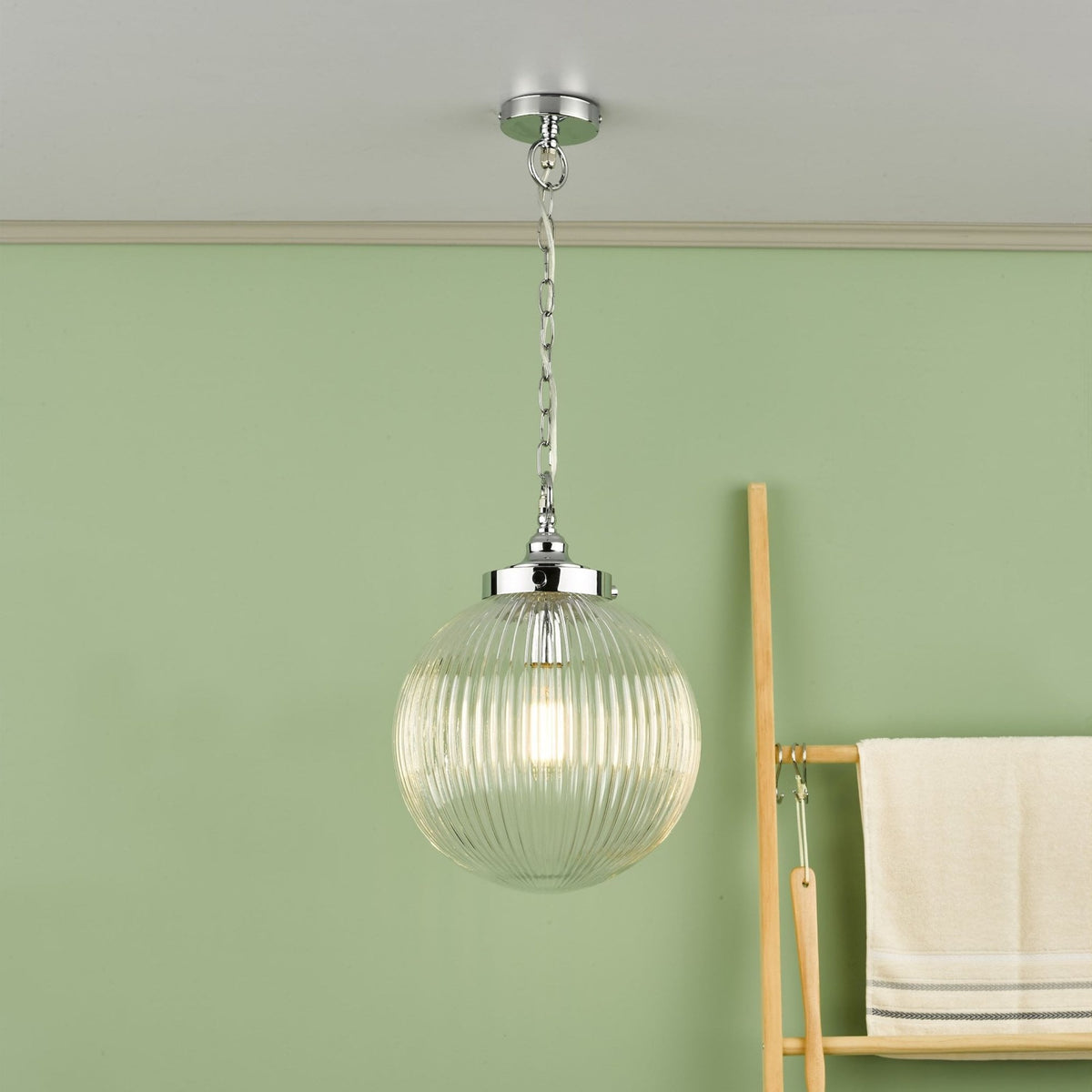 Ribbed glass globe pendant light with chrome accents, hanging from a ceiling against a green wall.