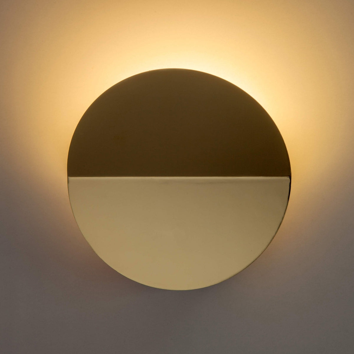 Round, bronze and brass wall light with a warm glow on the wall above.