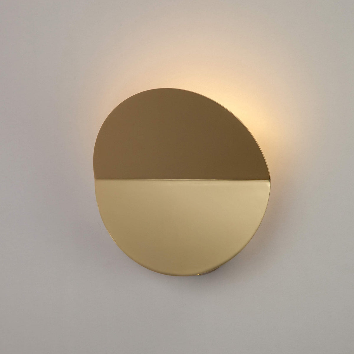Round, bronze and brass wall light with a warm glow on the wall above.