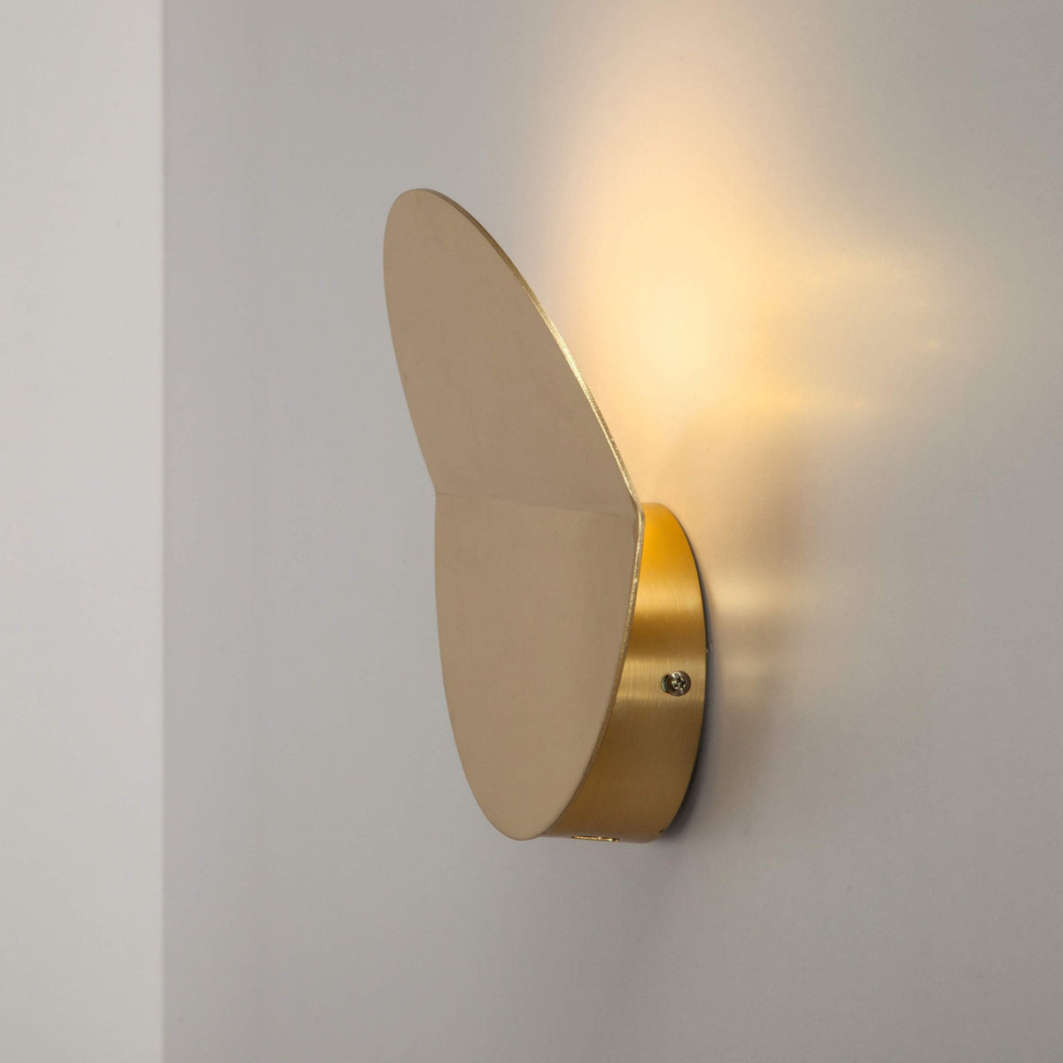 Side profile of a round, bronze and brass wall light with a warm glow on the wall.