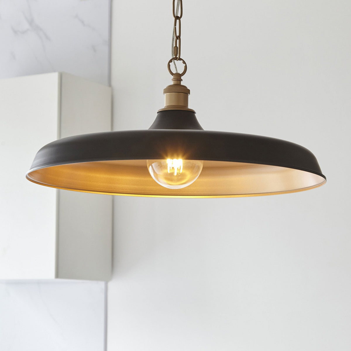 Un luminaire suspendu noir et or avec une ampoule exposée, éclairant une pièce de manière chaleureuse.
