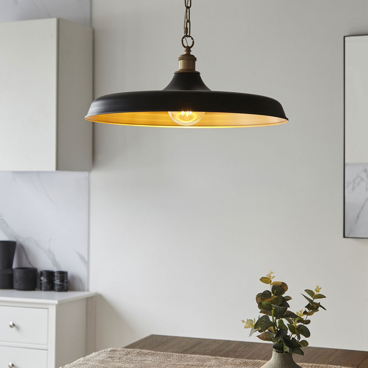 Un luminaire suspendu noir et or au-dessus d'une table, apportant une ambiance douce à la salle à manger.