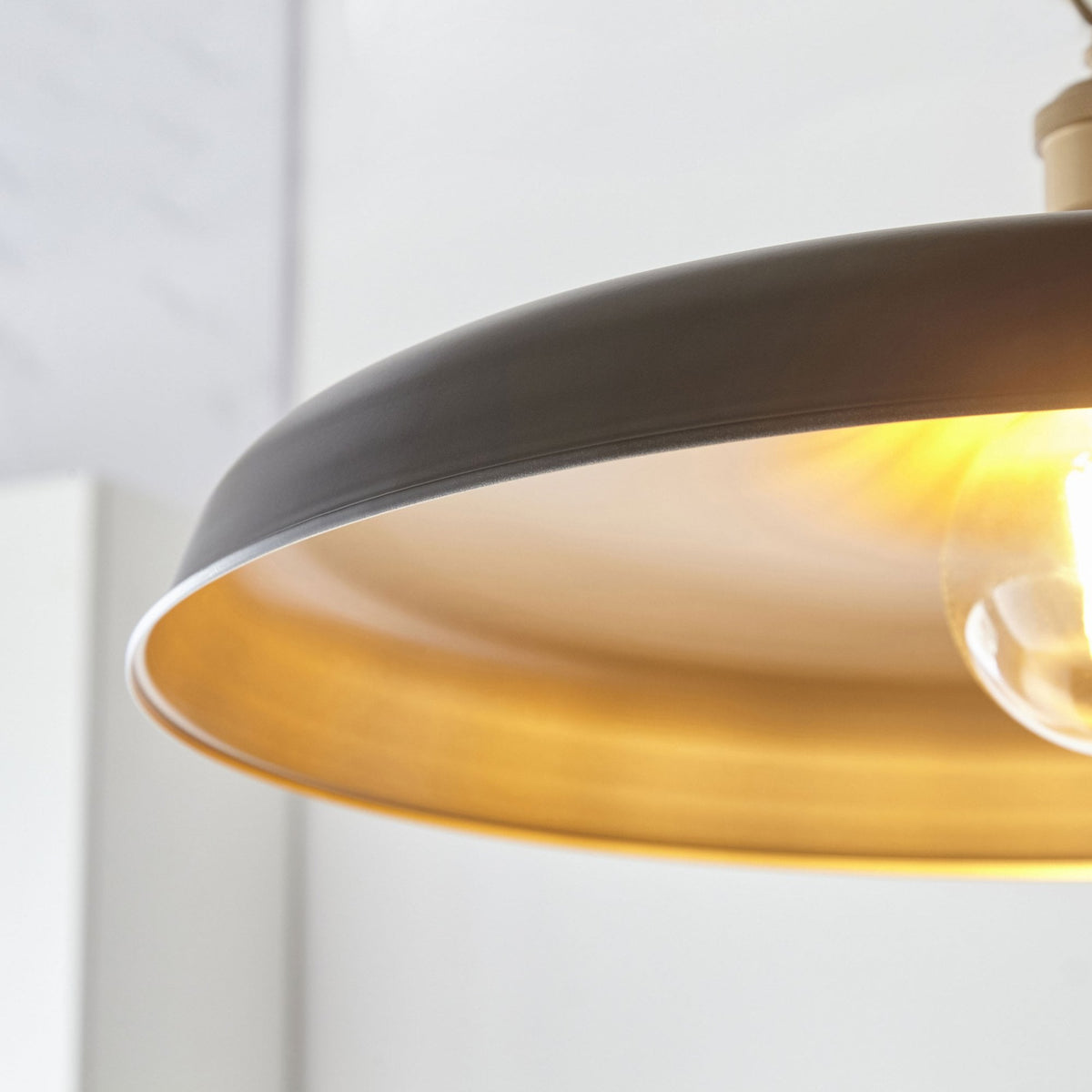 Gros plan d'un luminaire suspendu noir et or, montrant l'ampoule allumée et le reflet doré de la lumière.