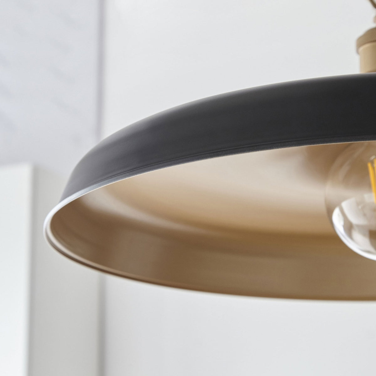 Détail d'un luminaire suspendu noir et or, mettant en valeur la finition métallique et la chaleur de l'ampoule.