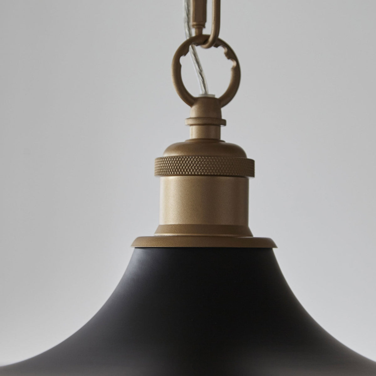 Gros plan du raccord et de la chaîne d'un luminaire suspendu noir et or, montrant les détails de conception.