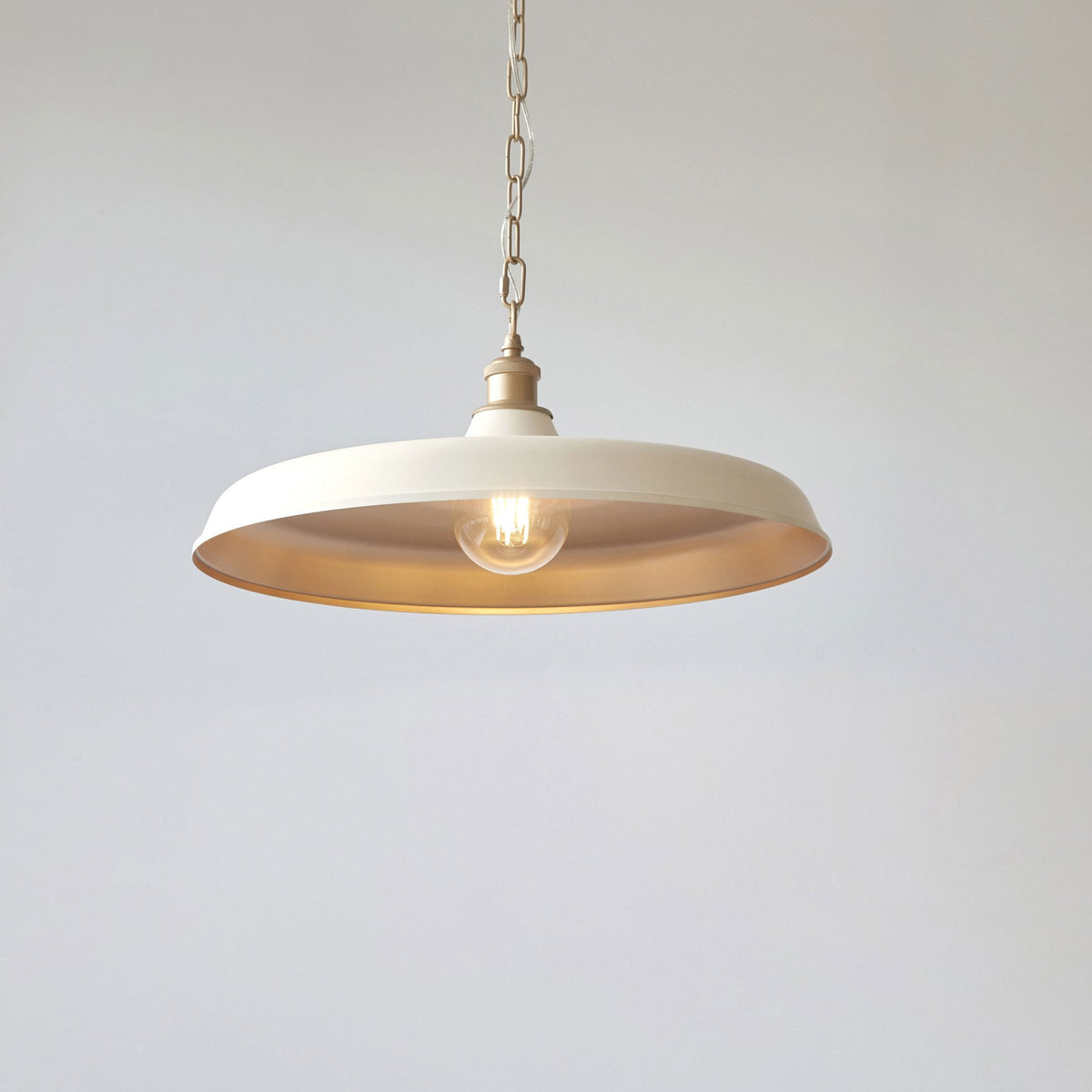 Cream-colored pendant light with a single bulb hanging against a white wall.