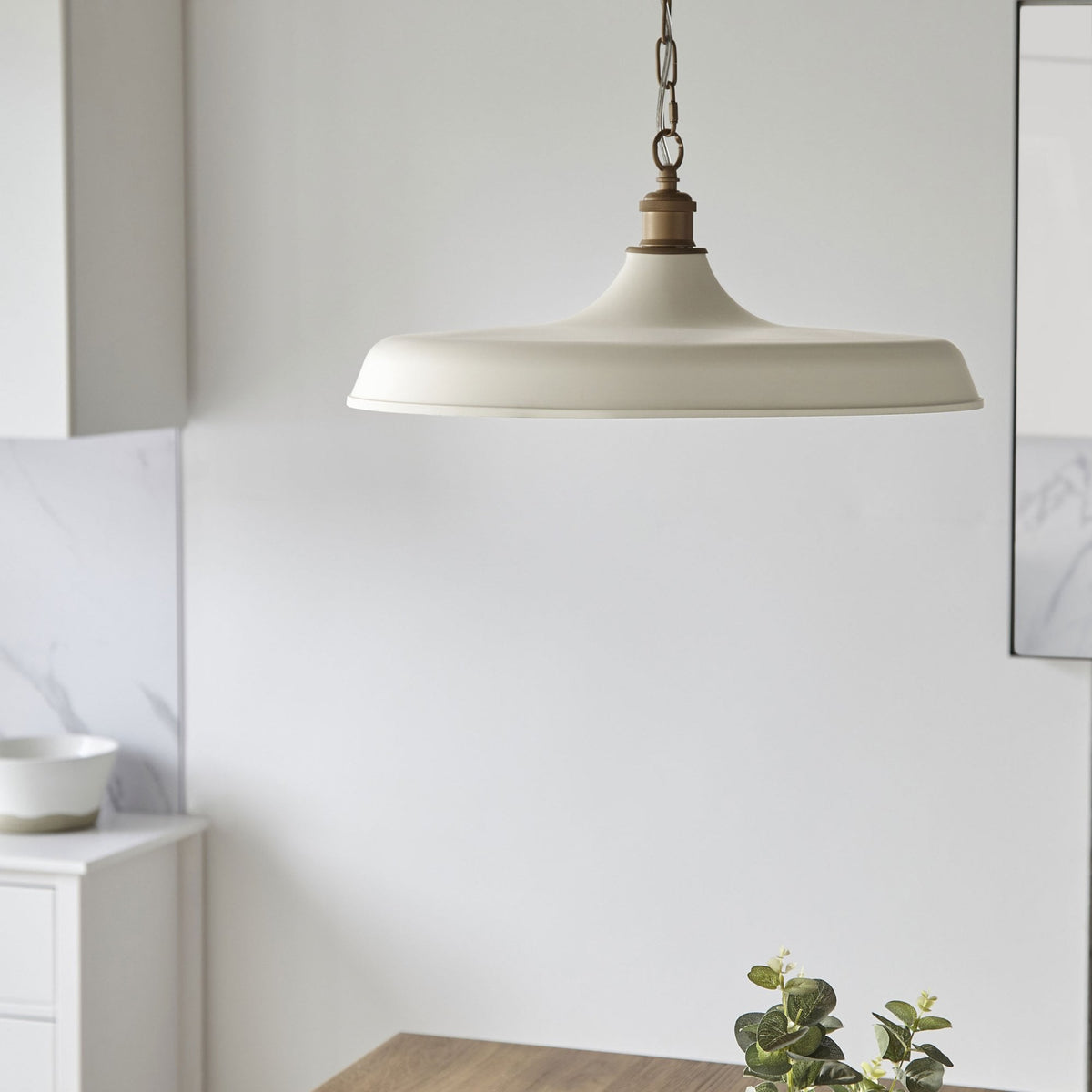 Cream-colored pendant light with a brass chain in a white room.
