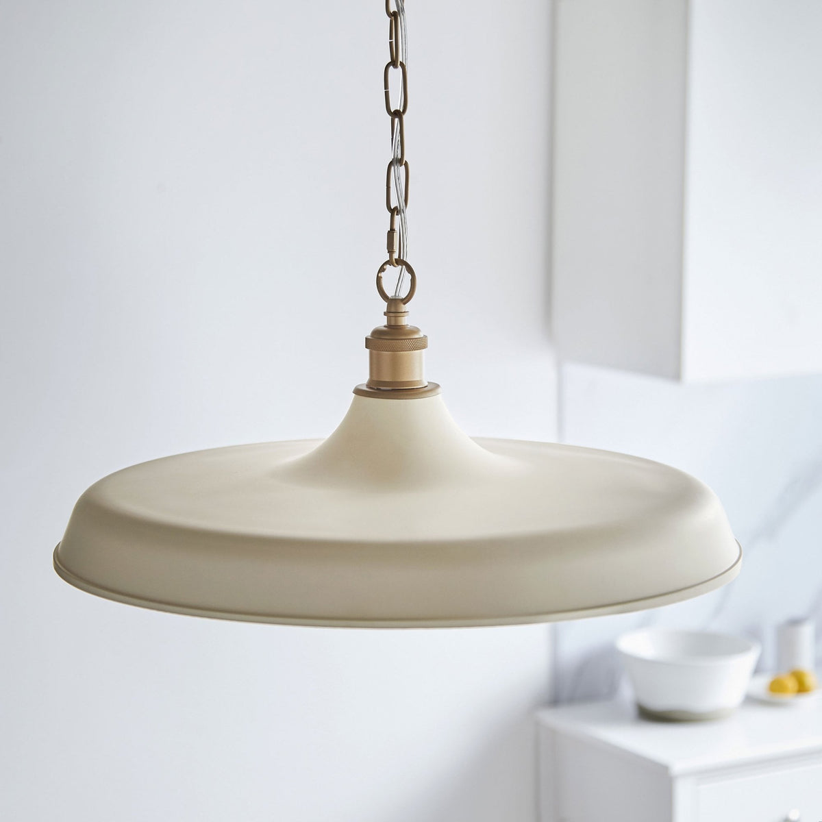 Cream-colored pendant light with a brass top and chain in a kitchen setting.