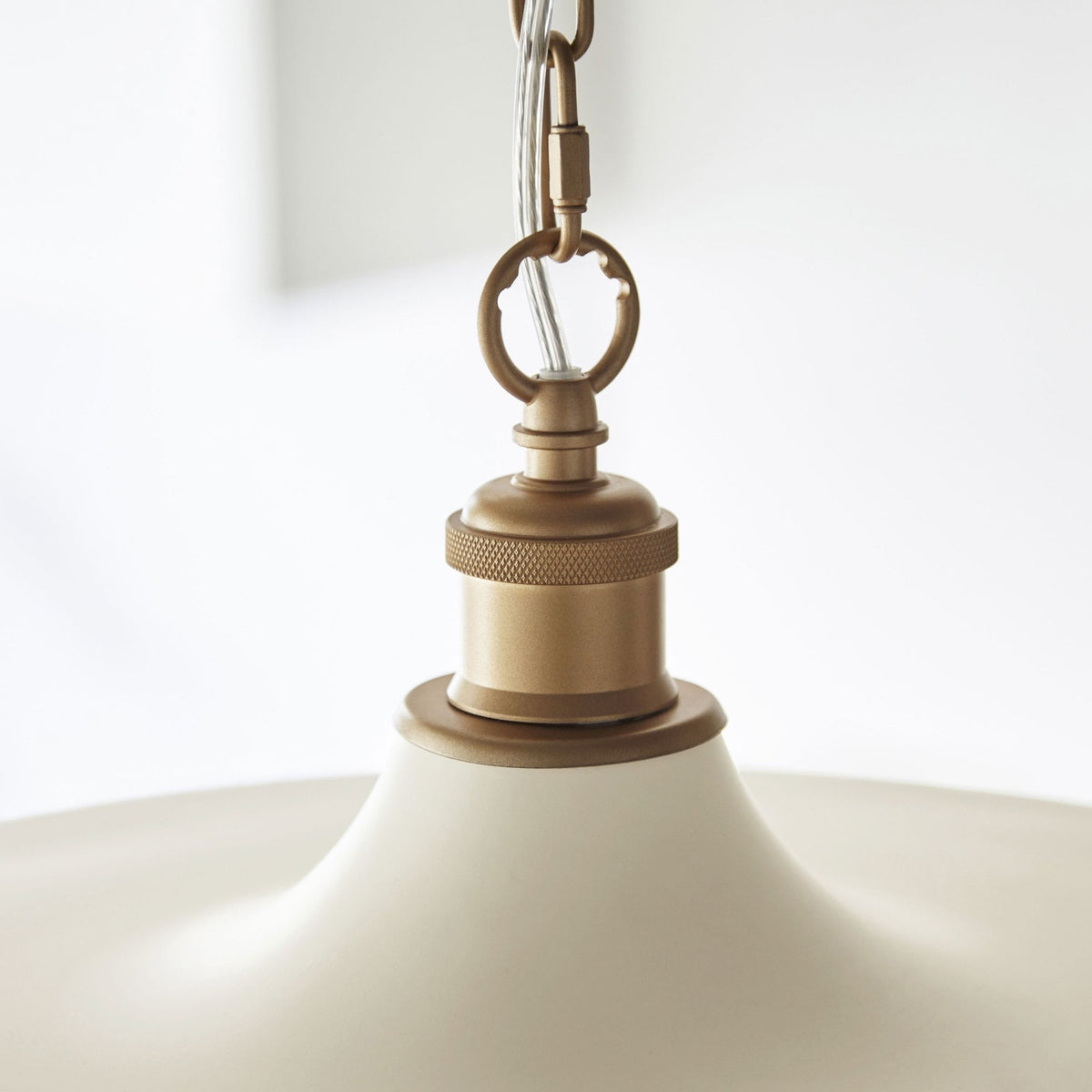 Close-up of the brass fixture at the top of a cream-colored pendant light.
