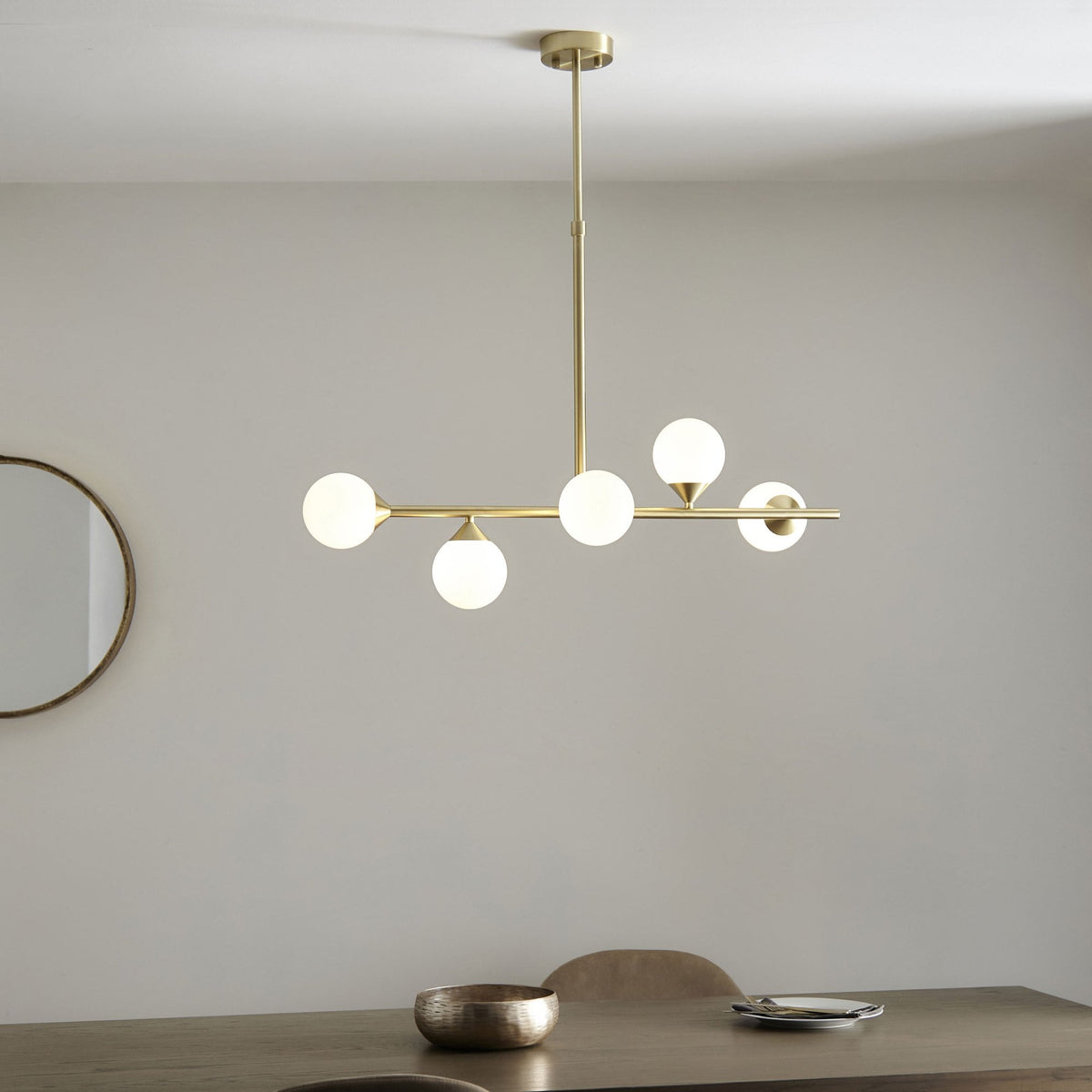 A five-light brass chandelier illuminates a dining table, enhancing a modern space with its elegant, warm glow.