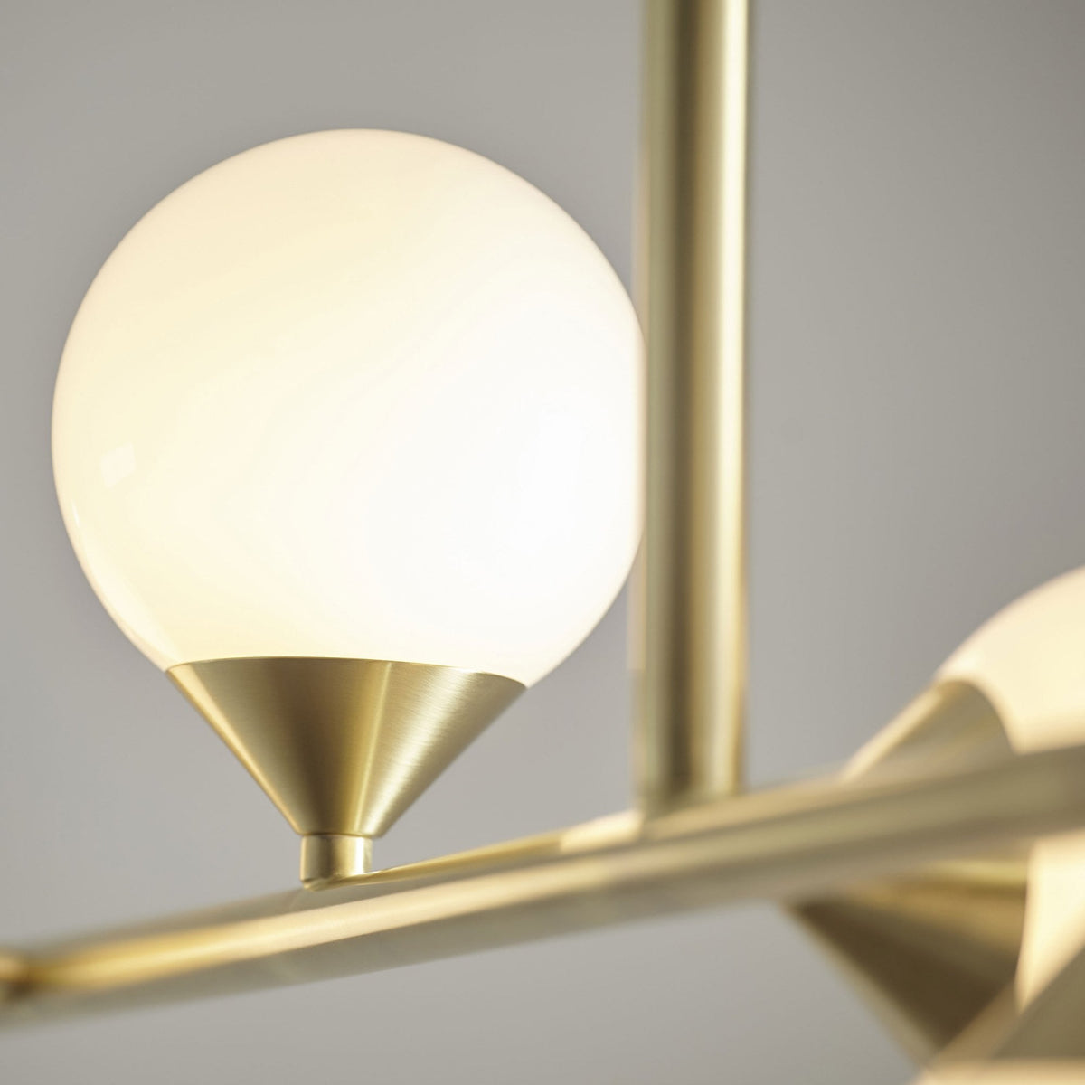 A close-up of a single brass globe light from a chandelier, emphasizing its sleek design and warm illumination.