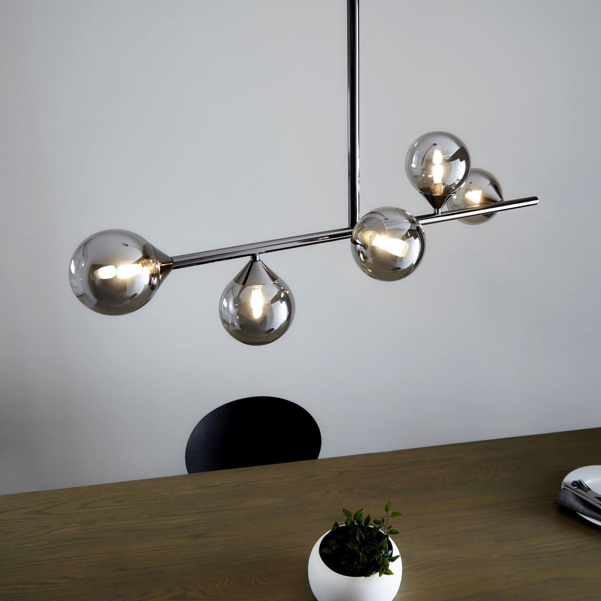 A modern chrome chandelier with five smoky glass globes, illuminating a wooden table below.