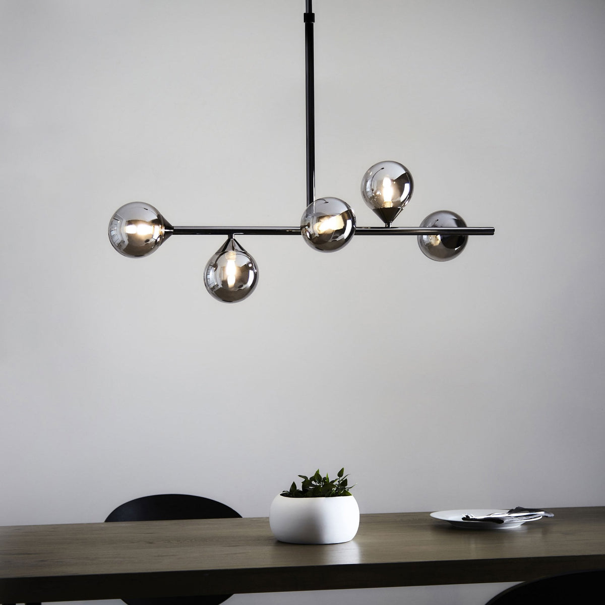 A contemporary black chandelier with five smoky glass globes hangs above a wooden dining table.