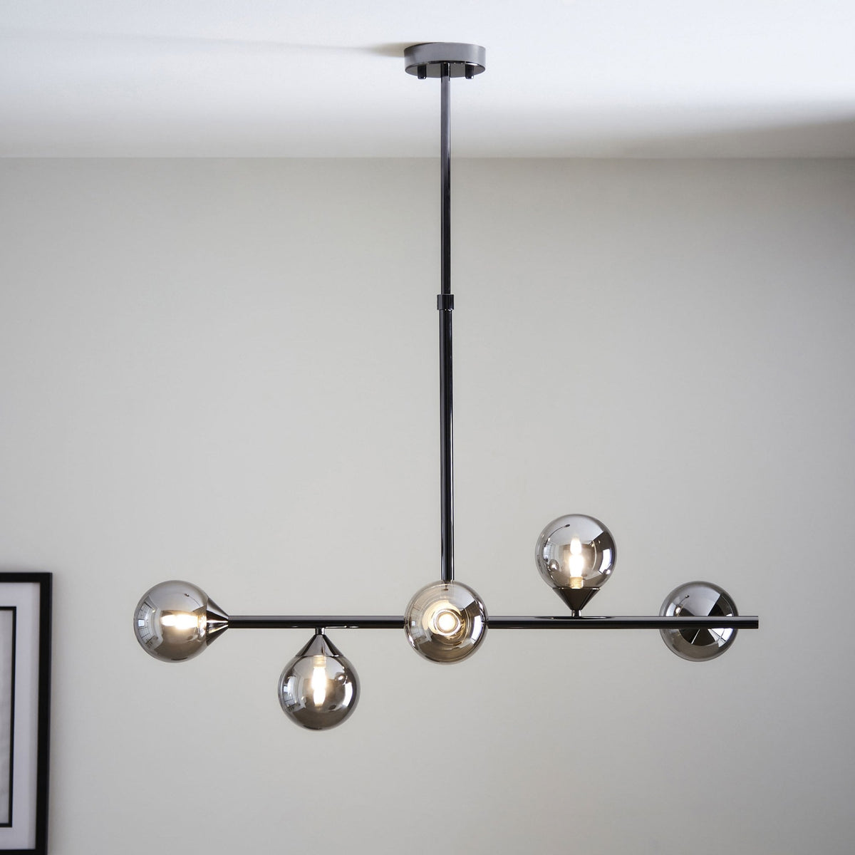 A modern black chandelier with five smoky glass globes, providing ambient light in a room.