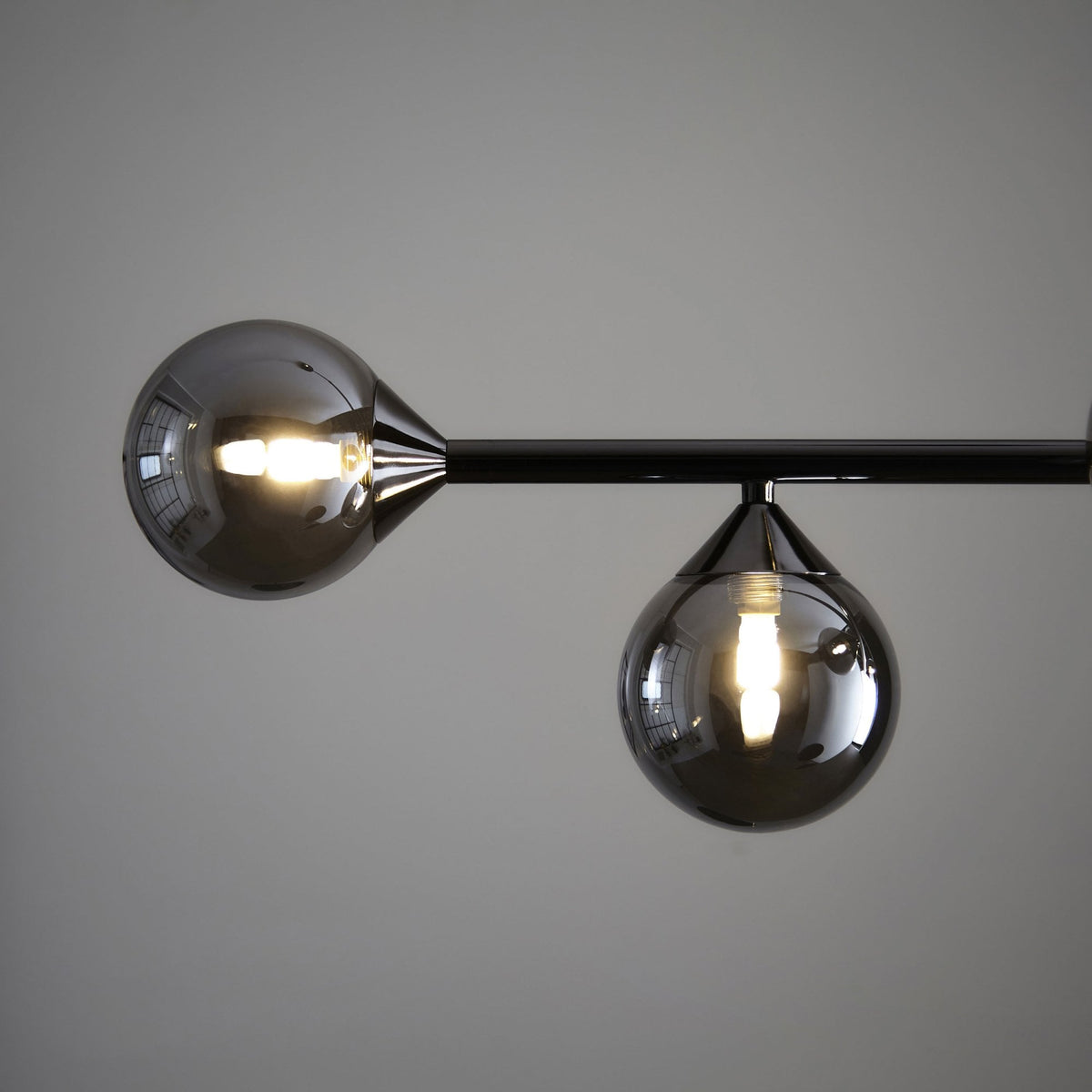 A close-up view of two smoky glass globes with visible light filaments, attached to a black bar.