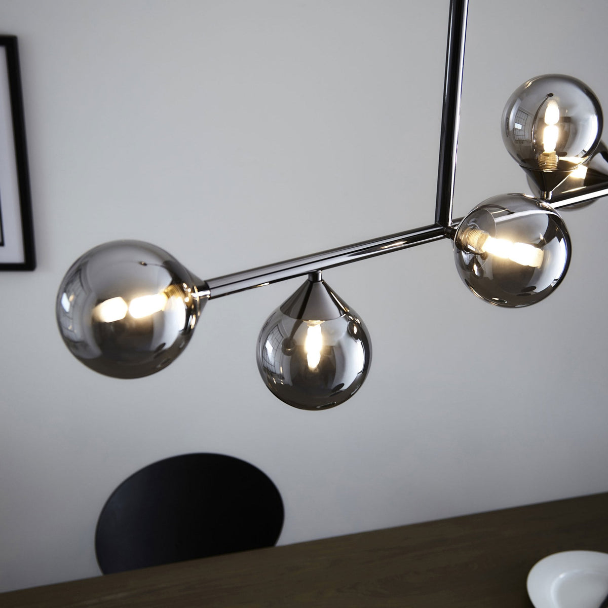 A modern chrome chandelier with smoky glass globes casting a warm glow over a wooden table.