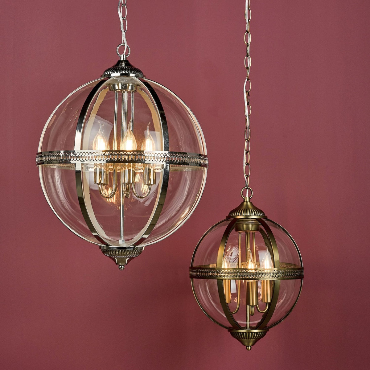 Two globe pendant lights, one silver and one brass, with exposed bulbs, hanging against a red wall.