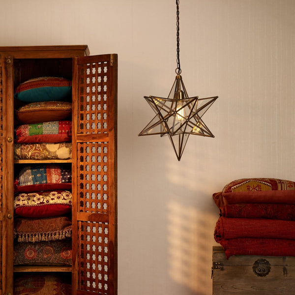 A star-shaped pendant light illuminates a wooden cabinet filled with colorful pillows and a stack of red textiles.