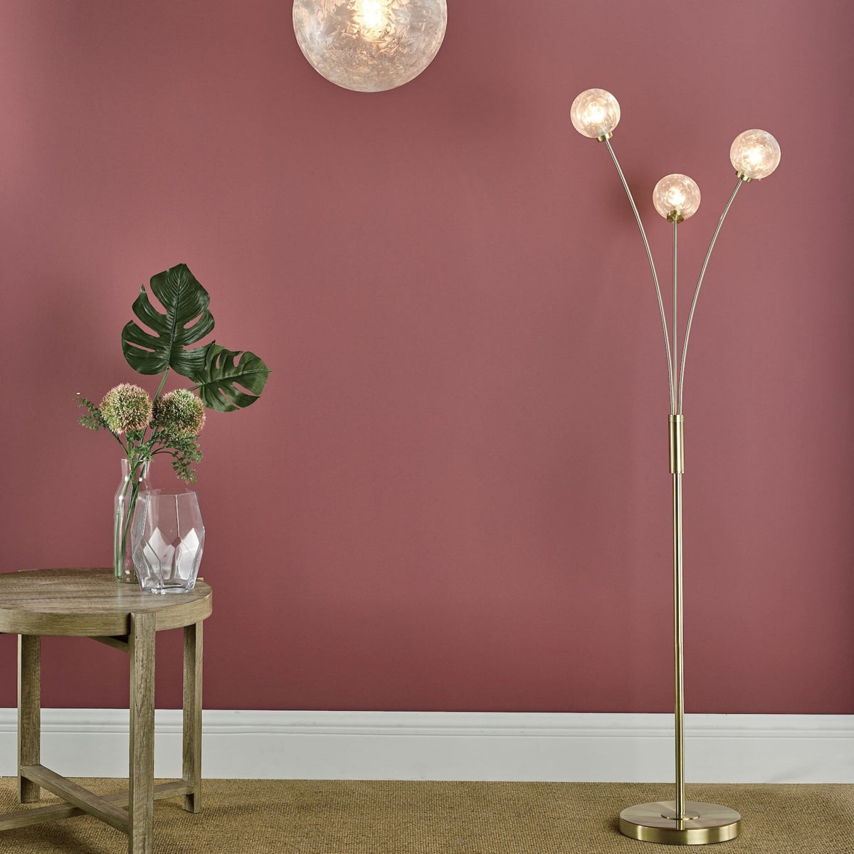 A gold floor lamp with three spherical lights next to a wooden side table with a vase of flowers.