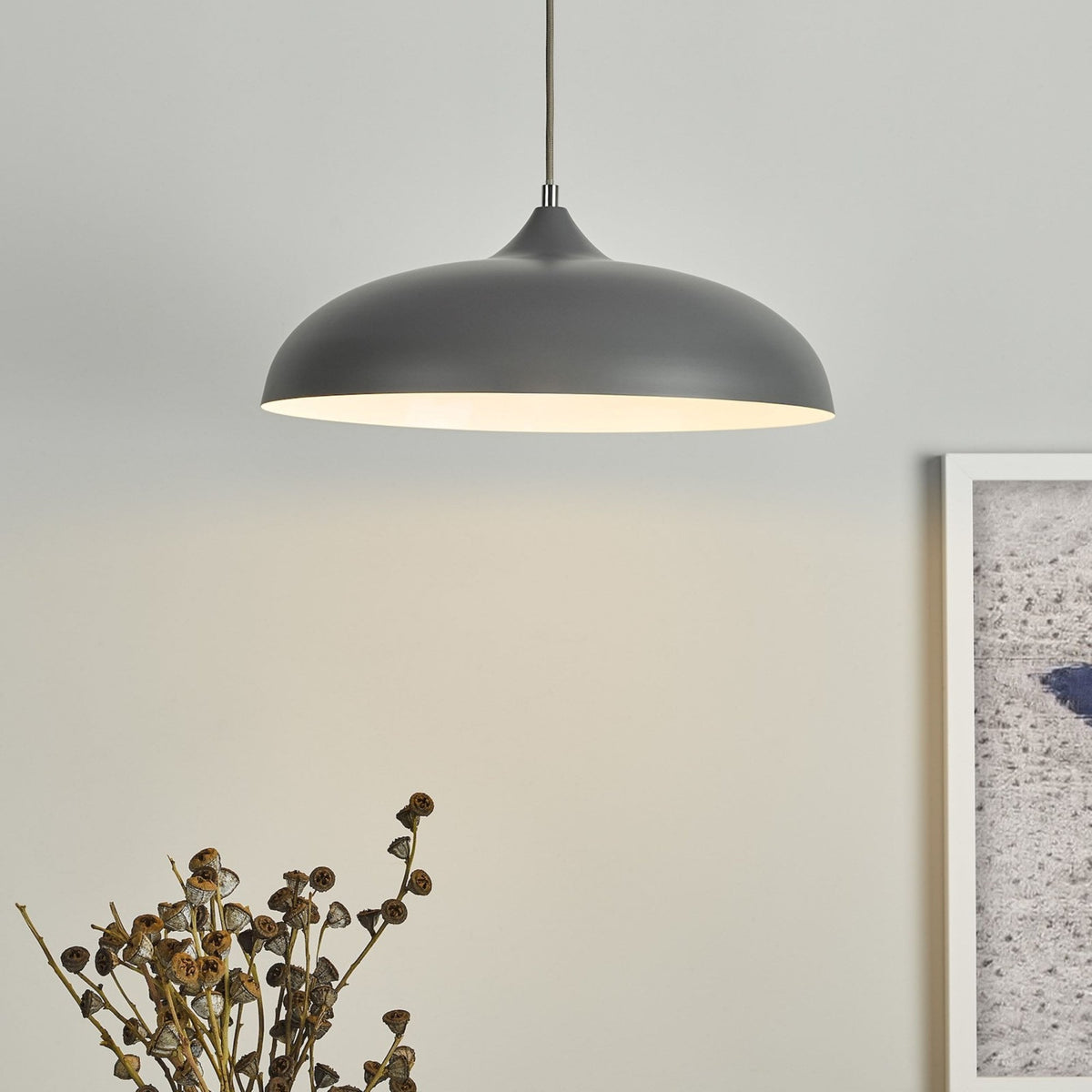 A gray pendant light illuminates a wall above dried seed pods and a framed picture.