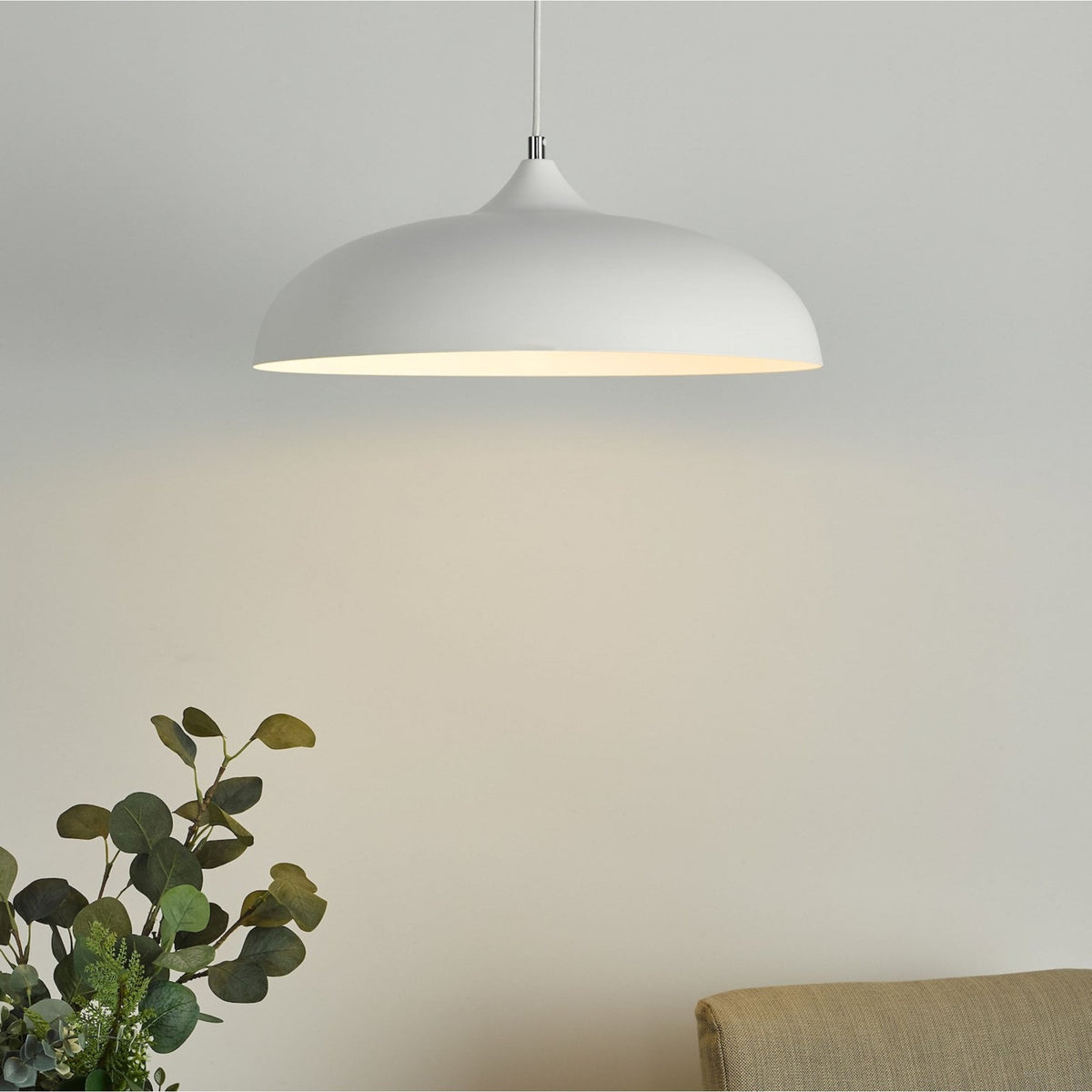 White dome pendant light illuminating a room with a plant and a couch.