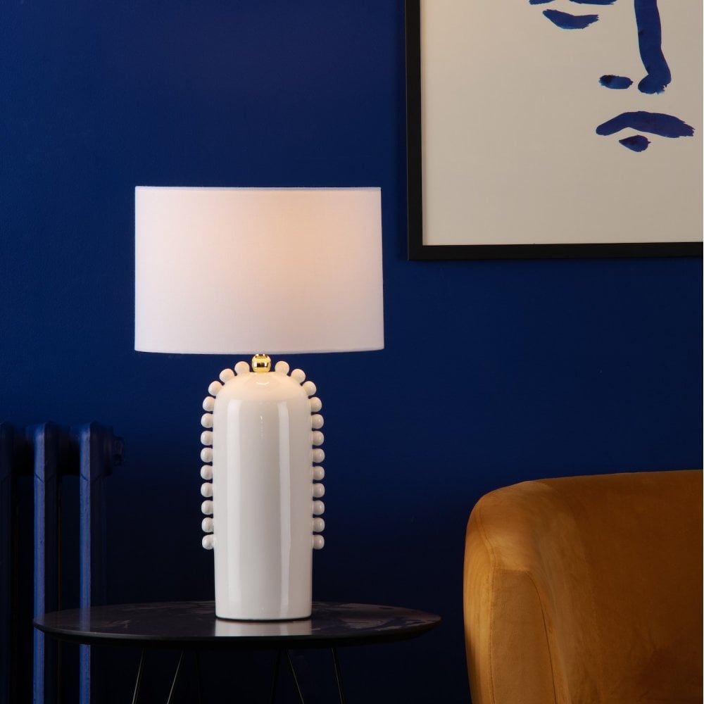 White ceramic table lamp with a textured base and white shade on a black table, against a blue wall.